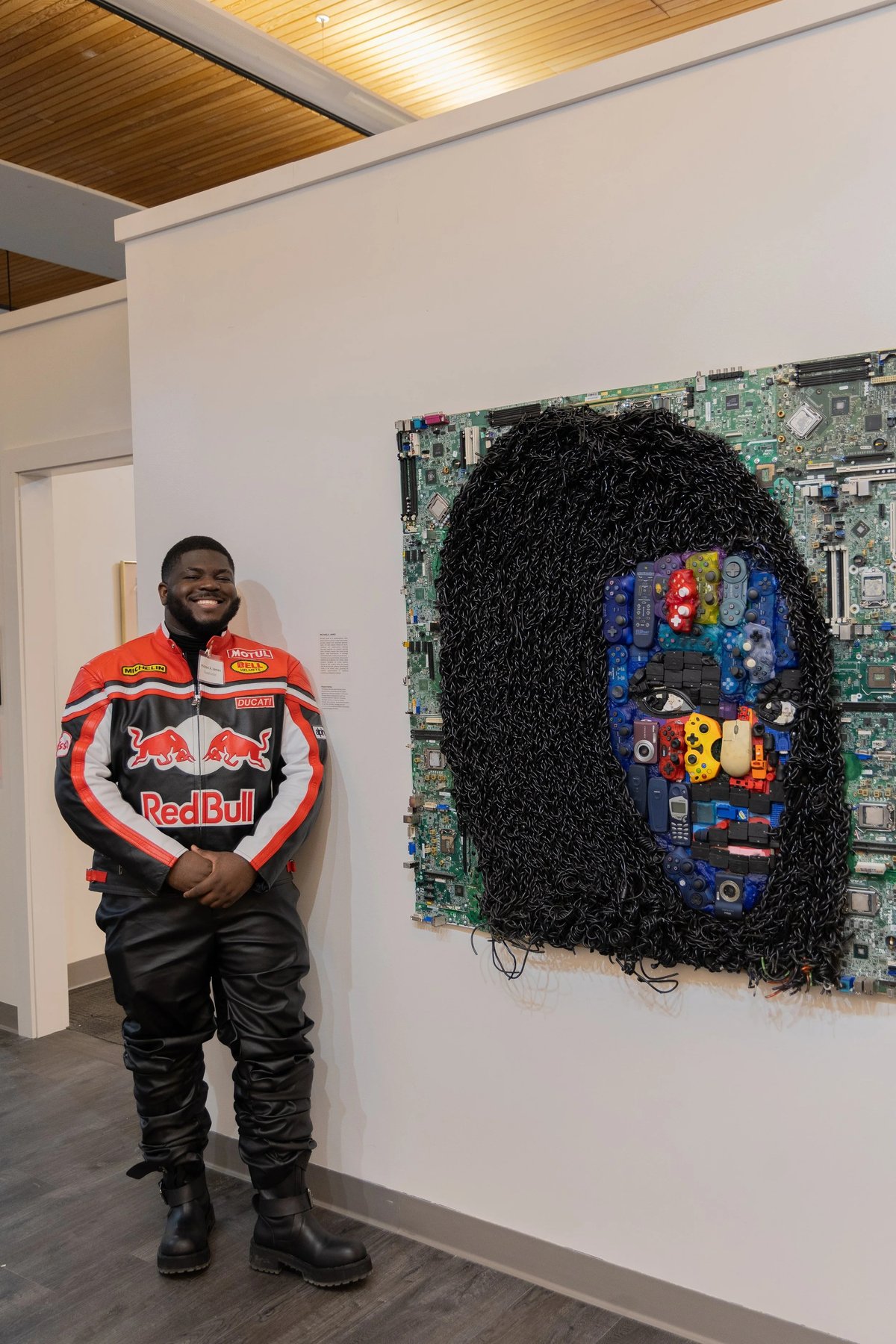 Michael Agwu standing beside one of his portrait mosaics made from motherboards and game controllers