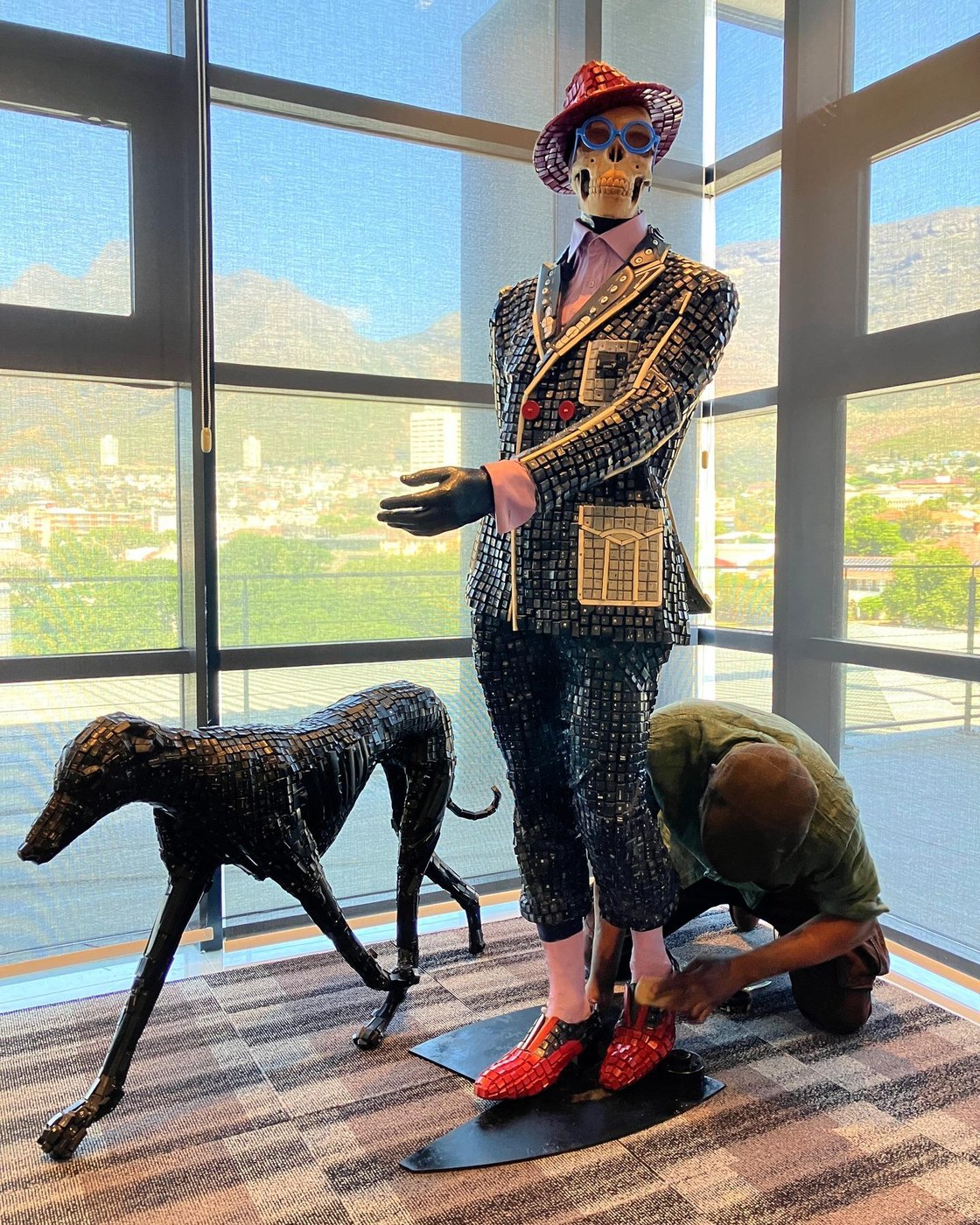 Maurice Mbikayi sculpture: Techno Dandy #10 (Surviving a Hostile Environment), a carved figure and hound made from wood, computer parts, fiberglass and resin
