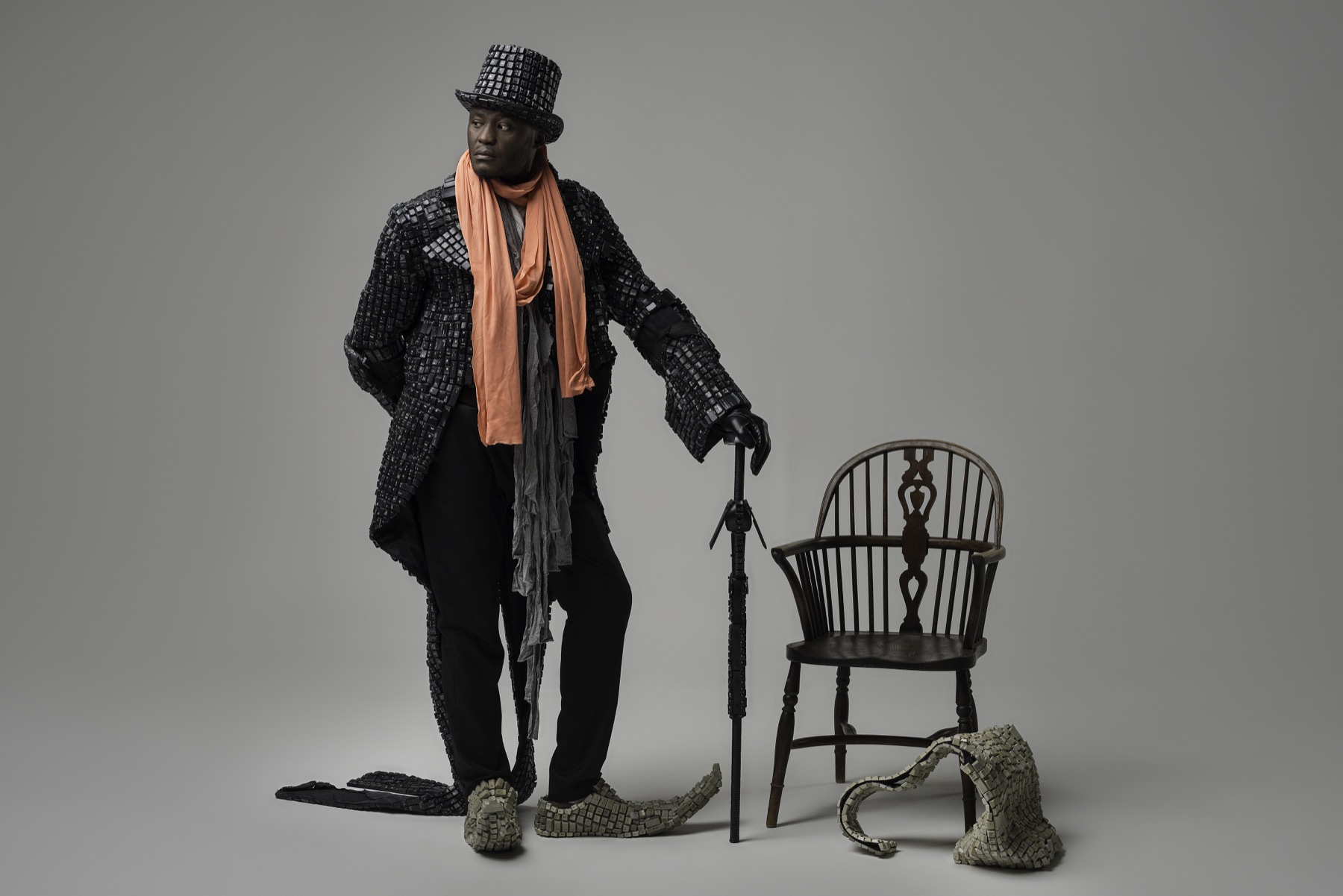 Maurice Mbikayi work: a standing figure in a keyboard-key coat and top hat beside a wooden chair