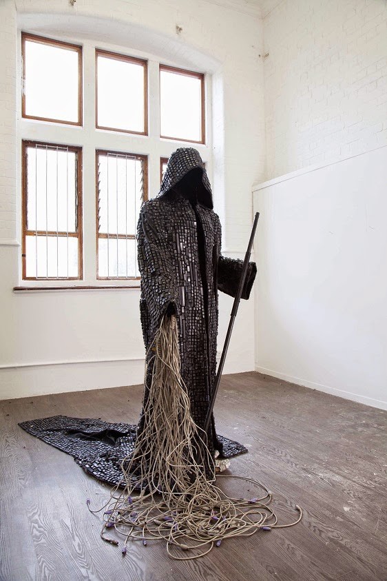 Maurice Mbikayi work: a hooded, robed figure made from keyboard keys, carrying a staff, with a long trailing cable train